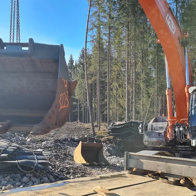 Stor gravemaskin med bøtte hevet på anleggsplass i skogen